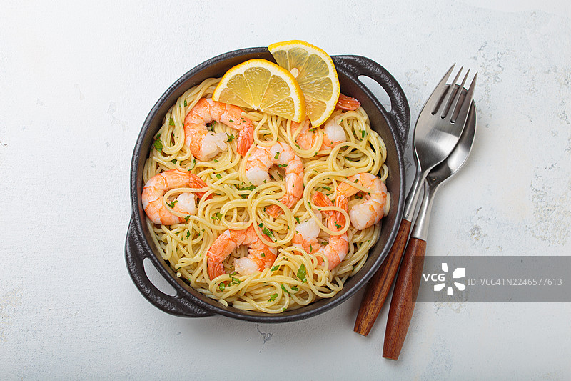 鲜美的鲜虾意大利面配新鲜柠檬片，盛在乡村风格的碗中，配有餐具，背景为浅色图片素材