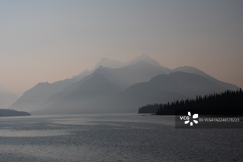 加拿大玛琳湖，傍晚时分宁静的山间湖泊风景，有薄雾笼罩的山峰和森林海岸线图片素材
