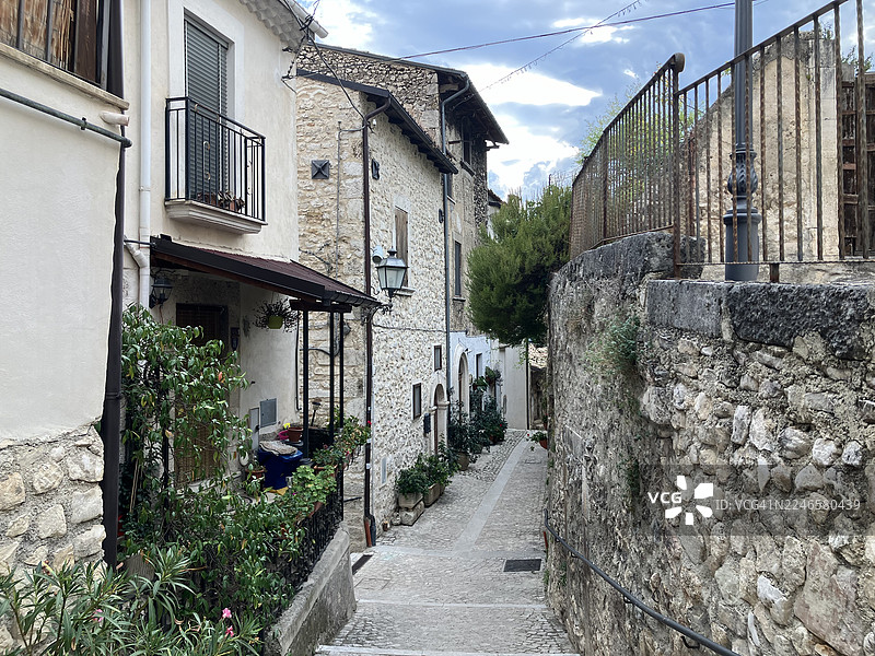 阴云密布的天空下，一条狭窄的鹅卵石小巷蜿蜒穿过欧洲古镇的历史悠久的石砌建筑。图片素材