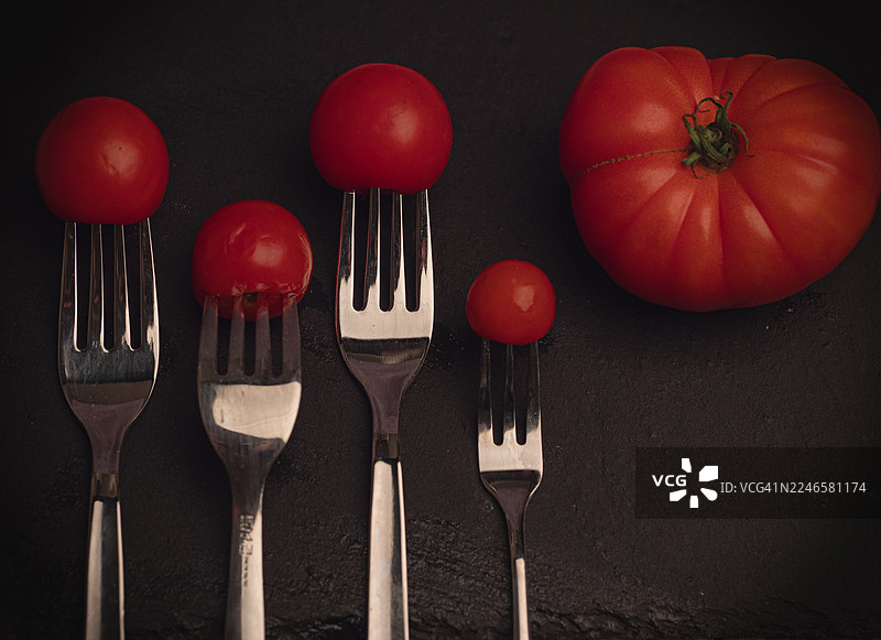 深色纹理背景下，新鲜的红番茄和叉子特写，展示了天然食材和厨房用具图片素材