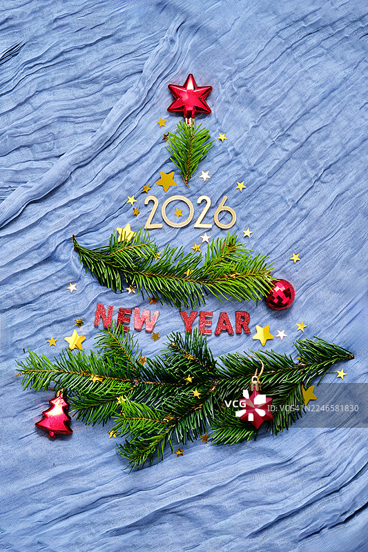 用杉树枝和装饰品制作的创意圣诞树，背景为蓝色织物，带有“新年2026”字样图片素材
