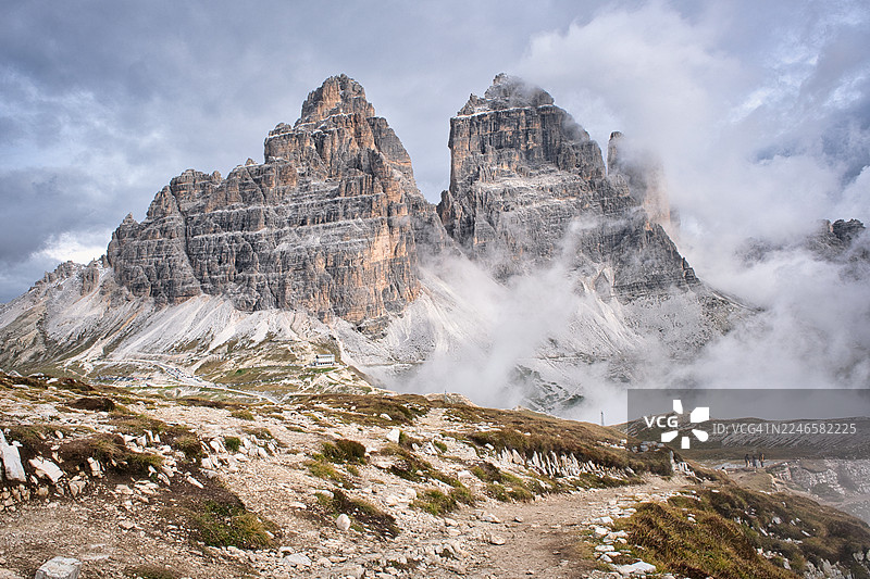 意大利，奥龙佐迪卡多雷，奥龙佐小屋，薄雾和云层笼罩的崎岖山峰的戏剧性山地景观，前景中有一条蜿蜒的小路图片素材