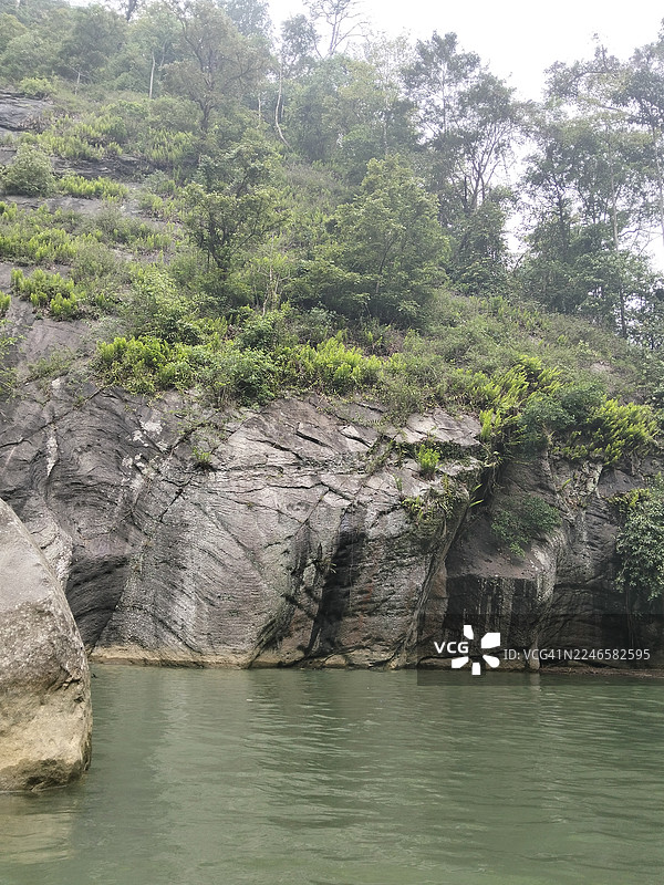 阴天之下，河水蜿蜒流过郁郁葱葱的岩石河岸森林的风景图片素材