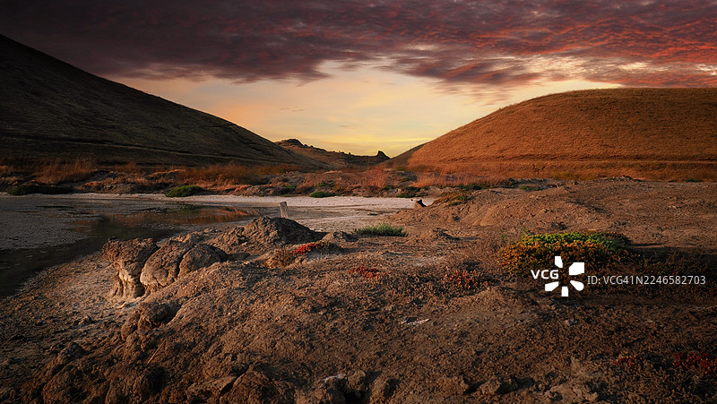 科罗拉多州弗里蒙特地区，戏剧性的日落映照着崎岖干旱的荒漠景观、连绵的山丘以及一小片水域图片素材