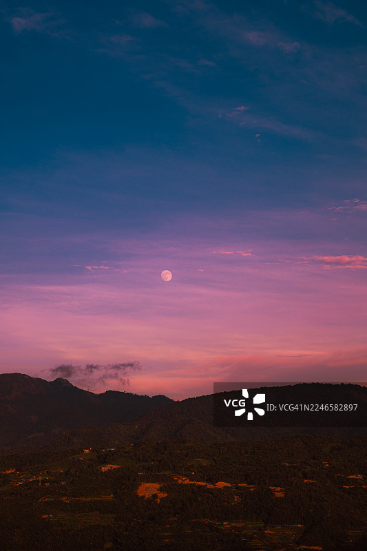 一轮满月照亮了宁静山景之上充满活力的暮色天空，展示了黄昏时大自然的美丽图片素材