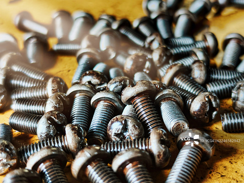 特写镜头：木质表面上堆叠着生锈的旧螺丝，突显了其纹理和细节。图片素材