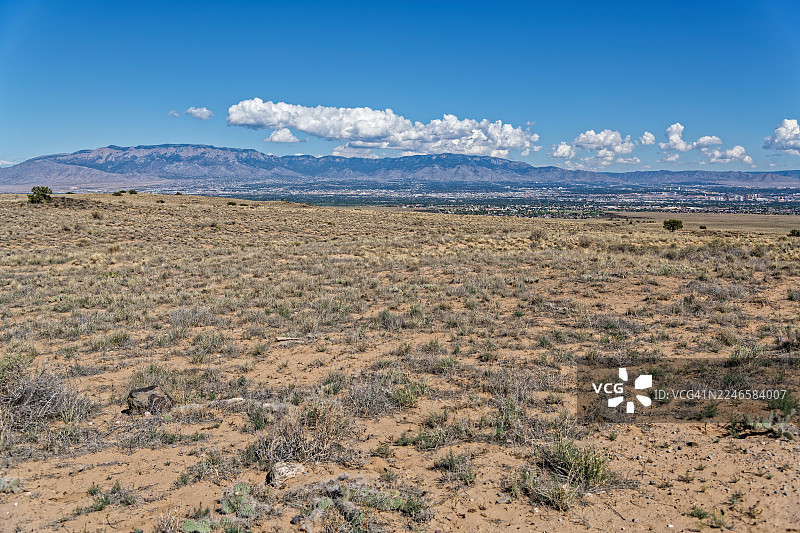 广阔的沙漠景观，远方有城市和山脉，天空湛蓝，点缀着白云，位于美国阿尔伯克基的佩特罗格里夫国家纪念碑图片素材