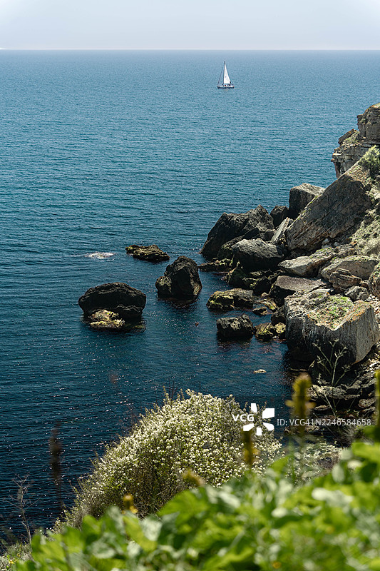 保加利亚，亚伊拉塔国家考古保护区，岩石海岸线与茂密绿植的地平线上的帆船图片素材