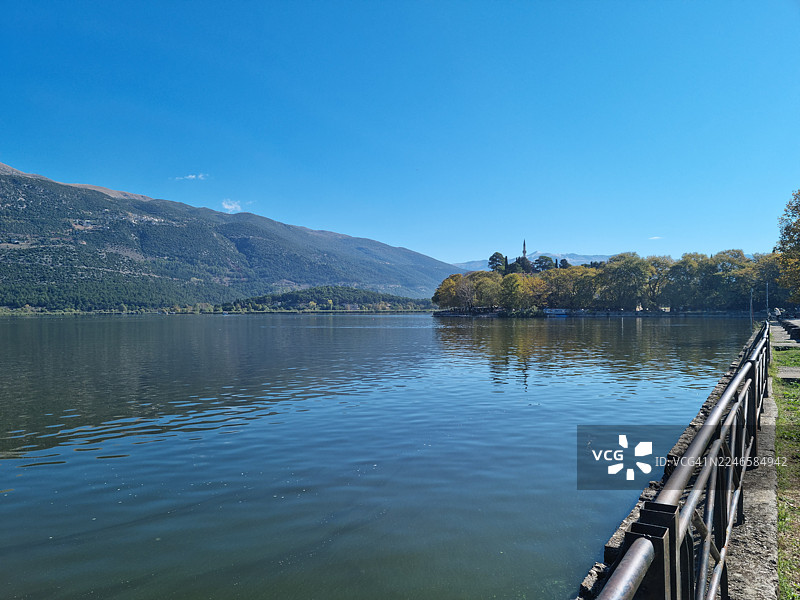 希腊伊奥尼纳，晴朗蓝天下宁静的湖泊与山峦景色图片素材