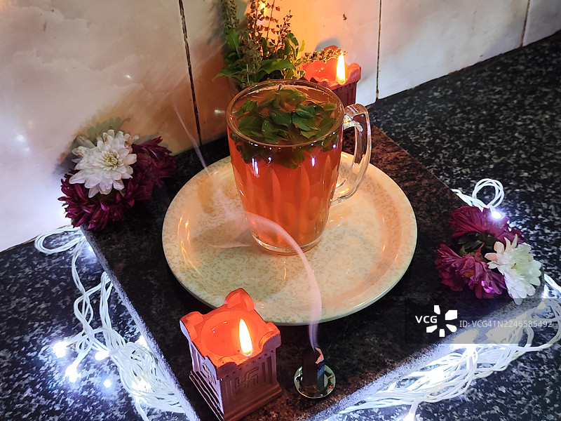 从高处俯瞰一杯草本薄荷茶，旁边摆放着点燃的蜡烛和串灯，在深色台面上营造出温暖放松的氛围图片素材