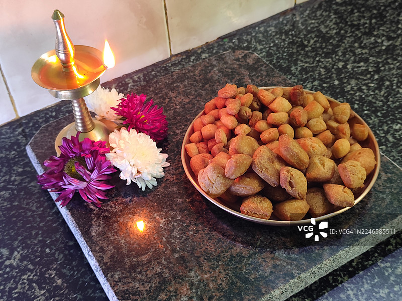 印度传统小吃Shankarpali，配以点亮的黄铜油灯和鲜花，象征着节日传统和家庭自制美食图片素材