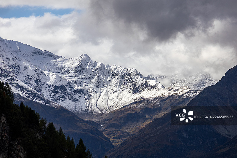 阴云密布的天空下，白雪皑皑的山脉呈现出戏剧性的壮丽景色图片素材