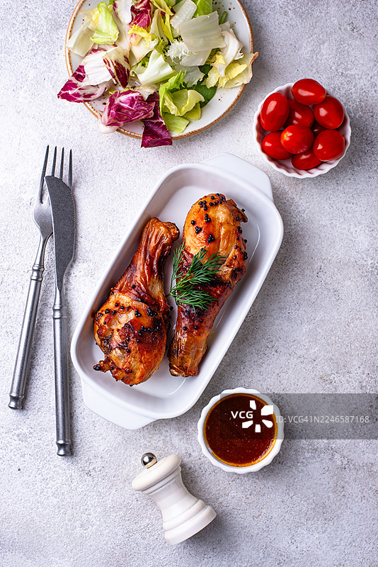 美味的烤鸡腿搭配新鲜沙拉、圣女果和酱汁，置于浅色背景上图片素材