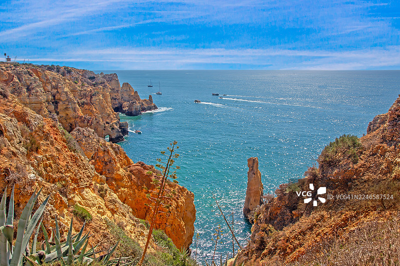 高角度俯瞰充满活力的蓝色大海与明亮天空，两旁是崎岖的海岸悬崖和岩石构造，远方有船只航行，葡萄牙图片素材