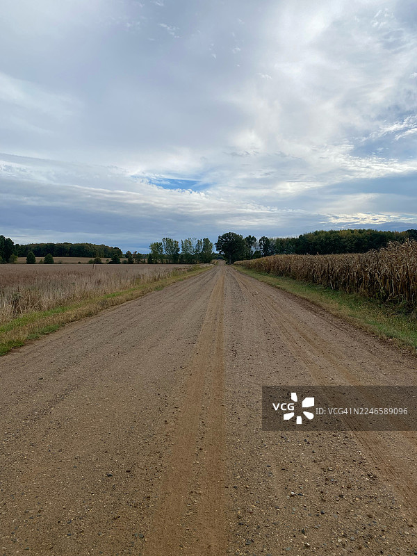 美国富尔顿，田野间一条尘土飞扬的土路在阴沉的天空下延伸图片素材