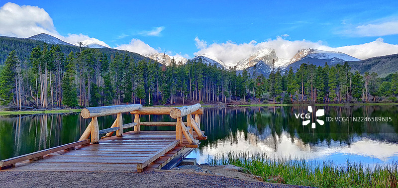 美国一处湖泊上的木质码头风景，背景有松树和雪山，天空湛蓝图片素材
