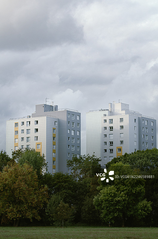 在多云的天空下，现代住宅楼矗立在茂密的绿树之上，展示了城市与自然的融合，法国图片素材