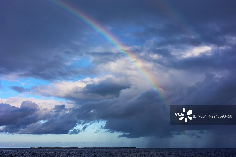 马尔代夫卡夫环礁，海面上空一道鲜艳的彩虹在戏剧性的云层天空下划过，景色壮丽图片素材