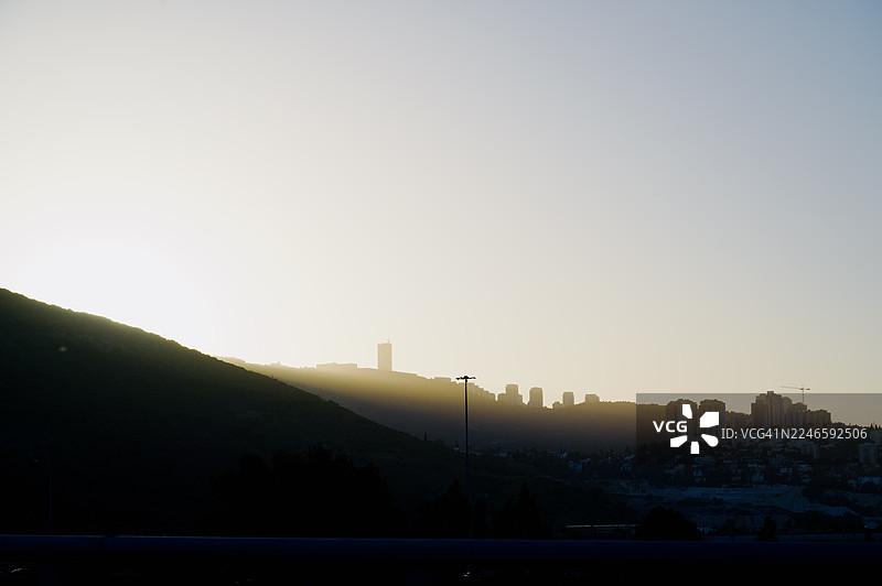 日落时分，剪影般的建筑和山丘在晴朗的天空中，散发着金色光芒，以色列海法图片素材