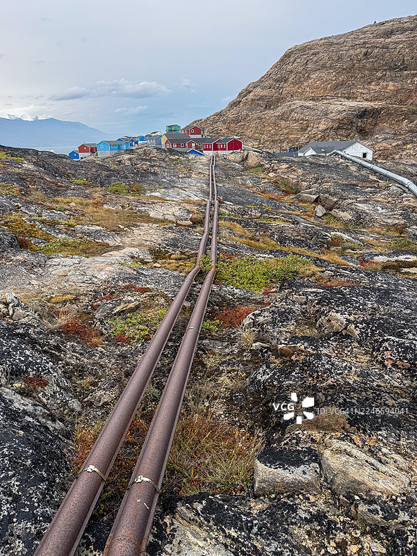 高角度拍摄的管道，向上延伸至岩石山坡，通往云层下的彩色村庄图片素材