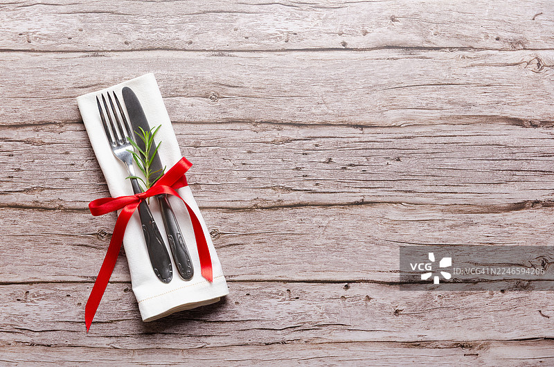 质朴的木桌上摆放着带有红色蝴蝶结和迷迭香的雅致餐具套装图片素材