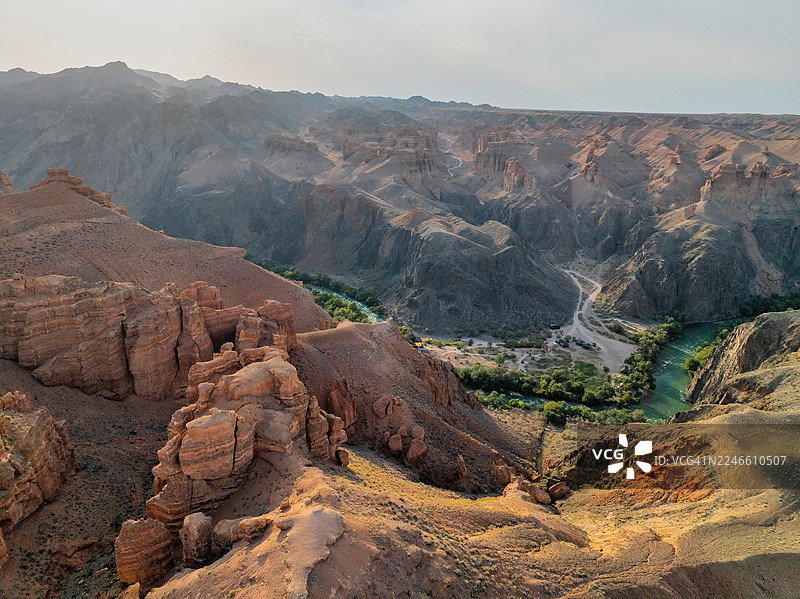 哈萨克斯坦查林峡谷近景，展示了下方蜿蜒道路上的车辆，以及高耸的红色岩石构造，在午后阳光的照耀下。图片素材