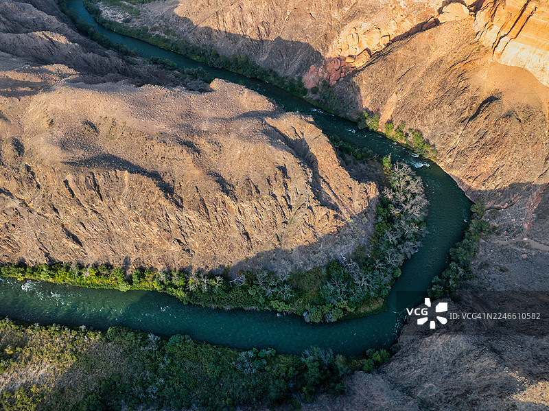 从中亚地区对恰林河急转弯处的极致俯瞰航拍，深邃的绿松石色河水与阳光照射和阴影下的岩壁形成鲜明对比。图片素材
