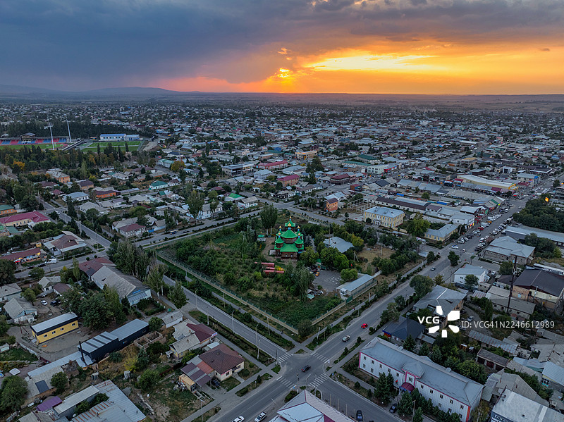 吉尔吉斯斯坦卡拉科尔的戏剧性日落航拍,展示了绿色圆顶的圣三一东正教教堂,在炽热的天空下被蔓延的低密度城镇所环绕。图片素材
