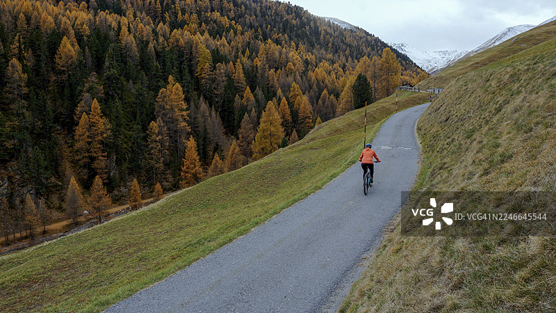 秋季，欧洲阿尔卑斯山，女子骑着电动自行车行驶在乡村道路上图片素材
