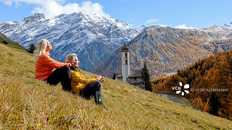 成熟夫妇在草地上，背景是教堂和远山图片素材