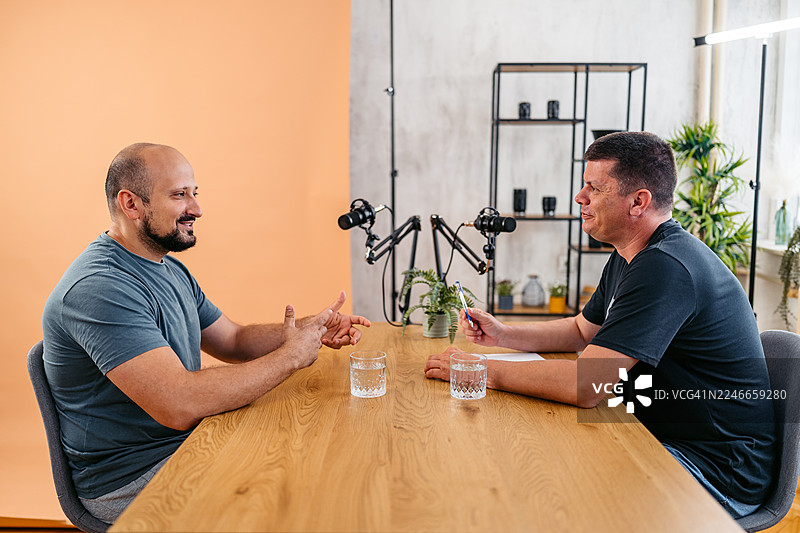 播客主持人与嘉宾在录音棚内对着麦克风交谈图片素材