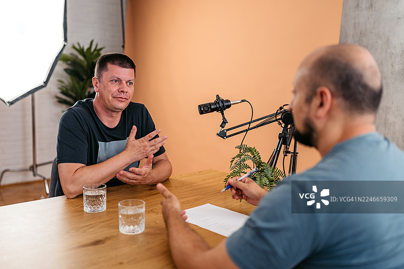 播客录音棚里，主持人与嘉宾正对着麦克风交谈图片素材