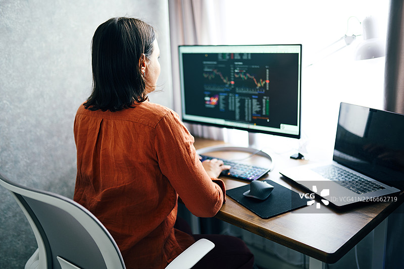 一位女士在现代家庭办公室的台式电脑显示器上分析股市数据图片素材