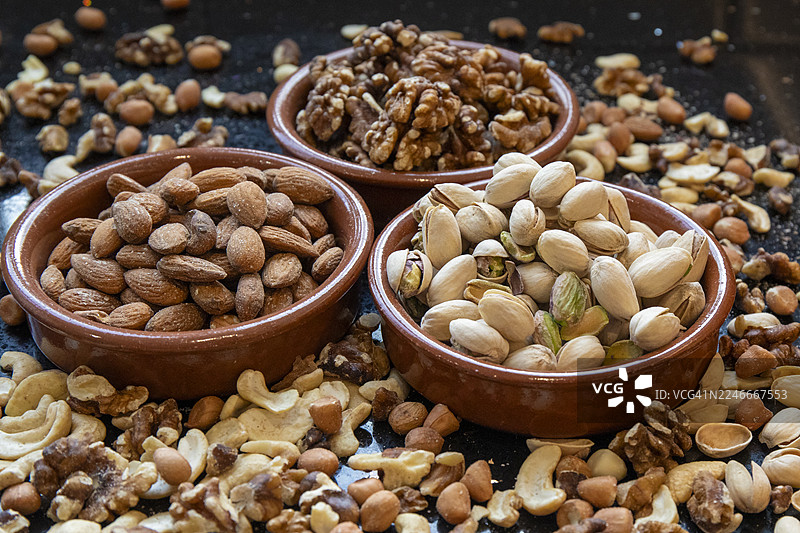 三个陶碗装着开心果、杏仁和核桃，周围散落着混合坚果。图片素材