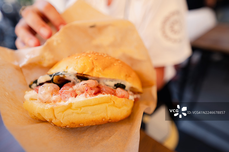 在法维尼亚纳，一个人拿着一份包含虾和贻贝的海鲜汉堡图片素材