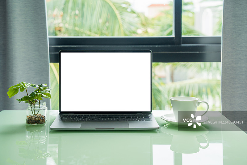 咖啡馆背景的桌子上放着一台屏幕空白的笔记本电脑。笔记本电脑屏幕留有复制空间。舒适的工作场所。正面视图。网上冲浪。视频会议。网上购物。图片素材