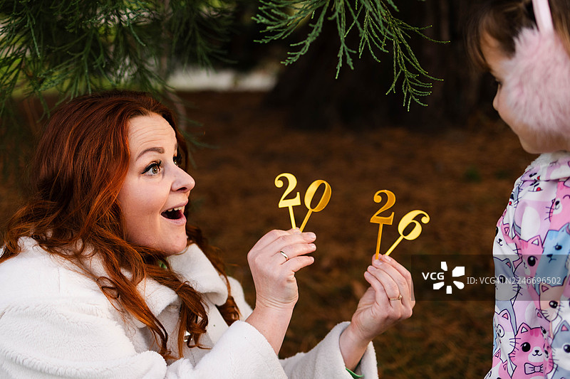 一位母亲在冬季假期期间，在户外向孩子展示2026的数字图片素材