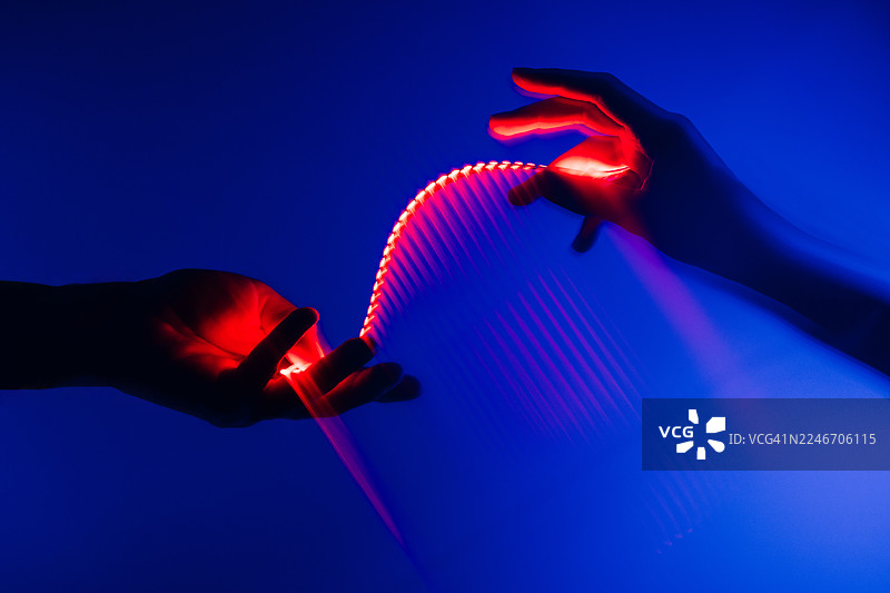 两只人手与发光的红色波浪线互动，在深蓝色背景上形成抽象、动态的连接。图片素材