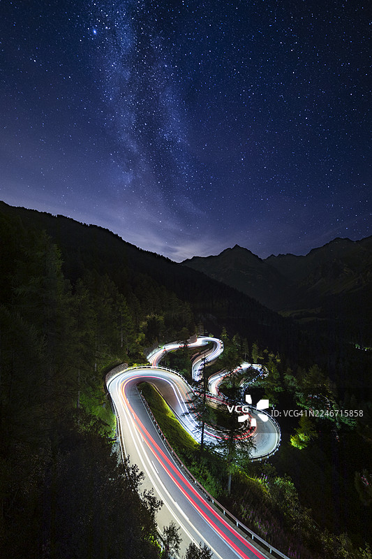 瑞士格劳宾登州上恩加丁马洛亚山口山路上，背景是银河的汽车尾灯图片素材