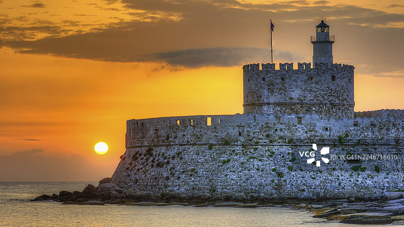 Agios Nikolaos 要塞，日出时分的金色光辉下的城堡与灯塔，背景是宁静的大海，联合国教科文组织世界遗产，罗得岛老城，罗得岛，佐泽卡尼群岛，希腊图片素材