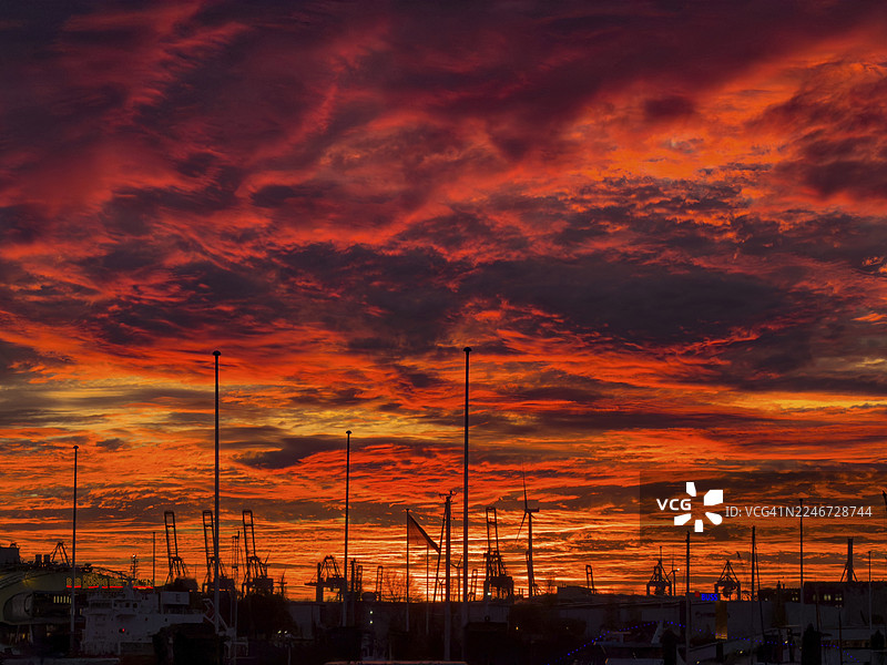 德国汉堡,汉堡港朗东桥(Landungsbrücken)戏剧性的日落天空,前景是起重机、船桅和风力涡轮机的剪影。图片素材