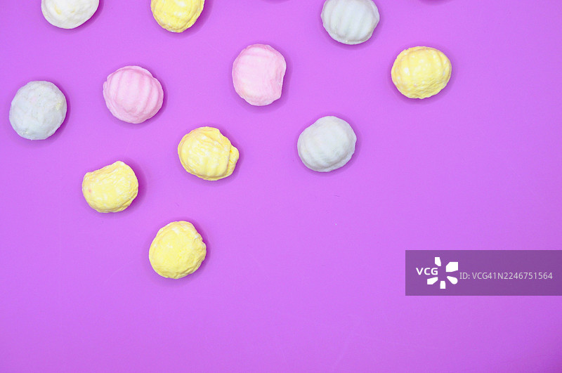 色彩缤纷的马卡龙蛋白霜饼干散落在鲜艳的紫色背景上，俯视角度，留有空白空间图片素材