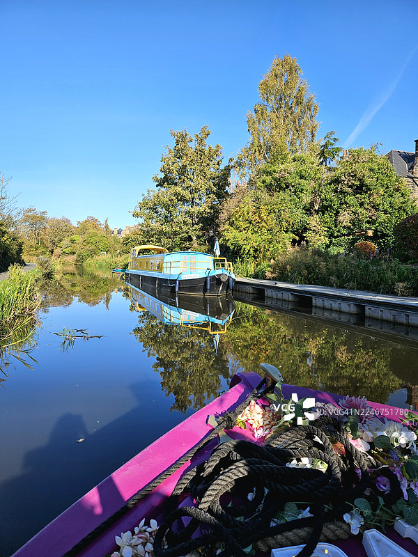 清澈蓝天下，色彩缤纷的船只与葱郁绿植点缀的运河美景图片素材