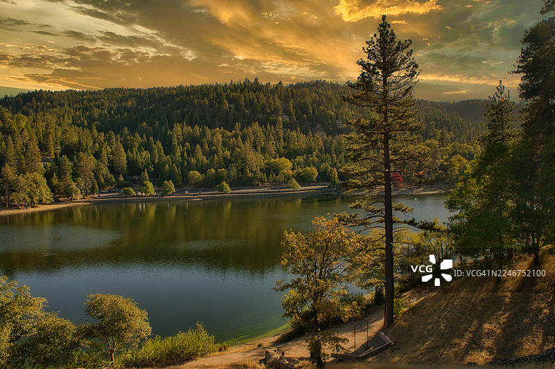 美国加利福尼亚州克雷斯特莱恩一处宁静湖泊的风景，湖泊被茂密的森林环绕，背景是壮丽的日落天空图片素材