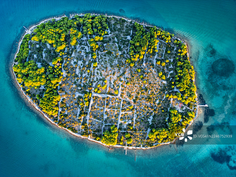 蔚蓝海水环绕的郁郁葱葱小岛的绝美鸟瞰图，岛上点缀着传统的干砌石墙和充满活力的绿树图片素材