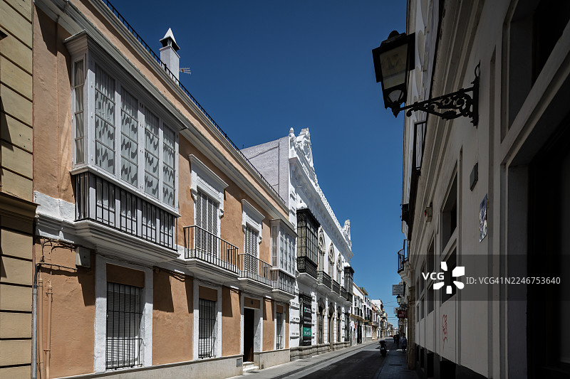 西班牙欧洲小镇狭窄街道旁的历史建筑低角度景观，晴朗蓝天下，普埃尔托街图片素材