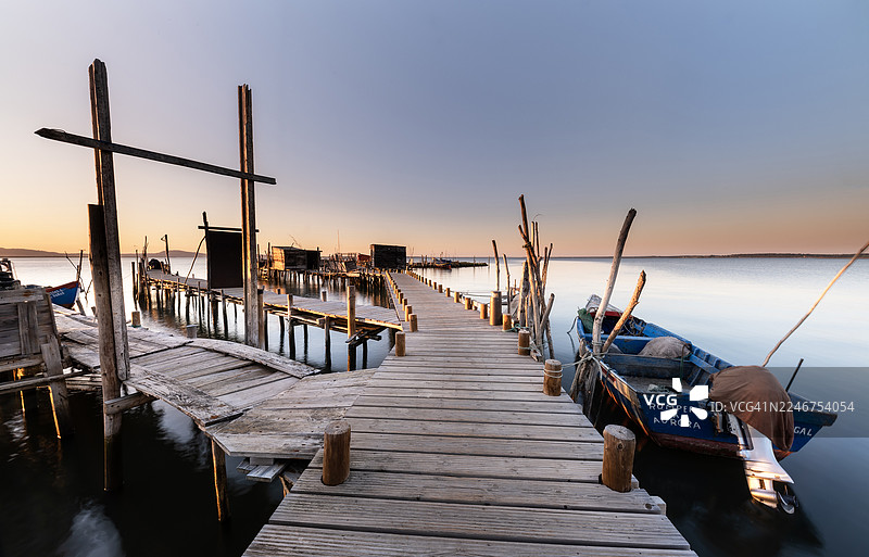 葡萄牙泻湖平静水面上的日落木制码头和传统渔船图片素材