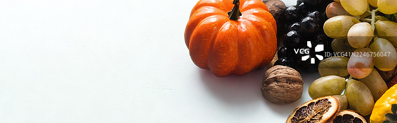 近距离拍摄的鲜艳南瓜、新鲜葡萄、核桃和干柑橘片，背景为纯净的白色，非常适合秋季和丰收主题图片素材