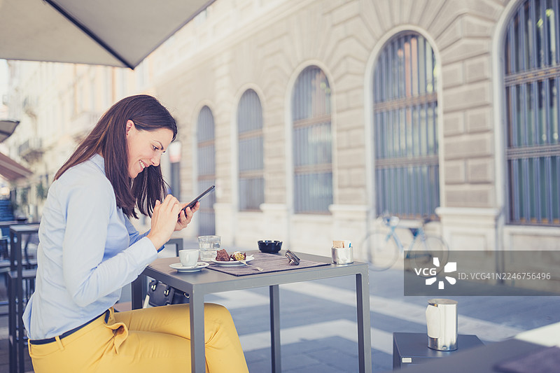 年轻女子在户外咖啡馆使用智能手机图片素材