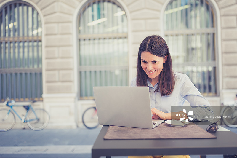 年轻女子在户外咖啡馆使用笔记本电脑工作图片素材